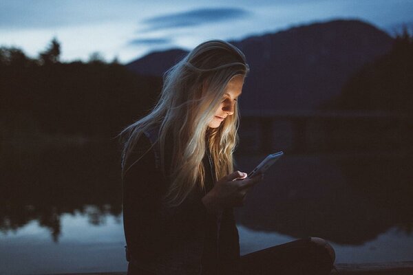 Girl sitting by a lake in the evening and scrolling her smartphone