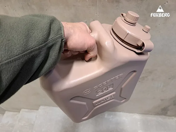 Main portant par la poignée un jerrican à eau militaire Scepter de 20 L couleur sable