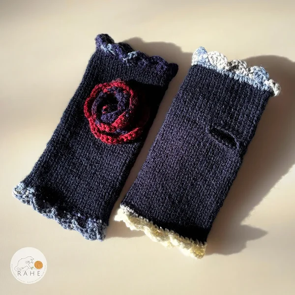 Hand-knitted navy blue fingerless gloves with lace edging, a crocheted flower and thumb opening – elegant Nordic handmade design in contrasting colours.