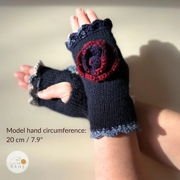 Hand-knitted navy blue fingerless gloves with lace edging, a crocheted flower and thumb opening, worn on a model – hand circumference 20 cm (7.9").
