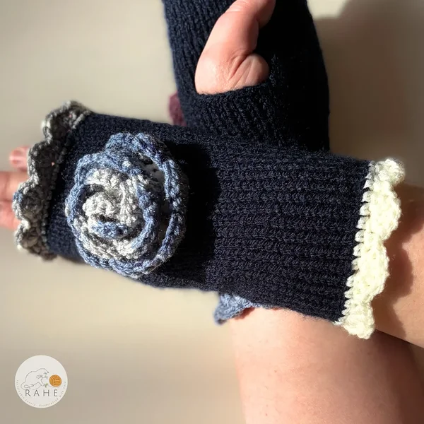 Hand-knitted navy blue fingerless gloves with lace edging, a crocheted flower and thumb opening – classic Nordic handmade design in contrasting colours.