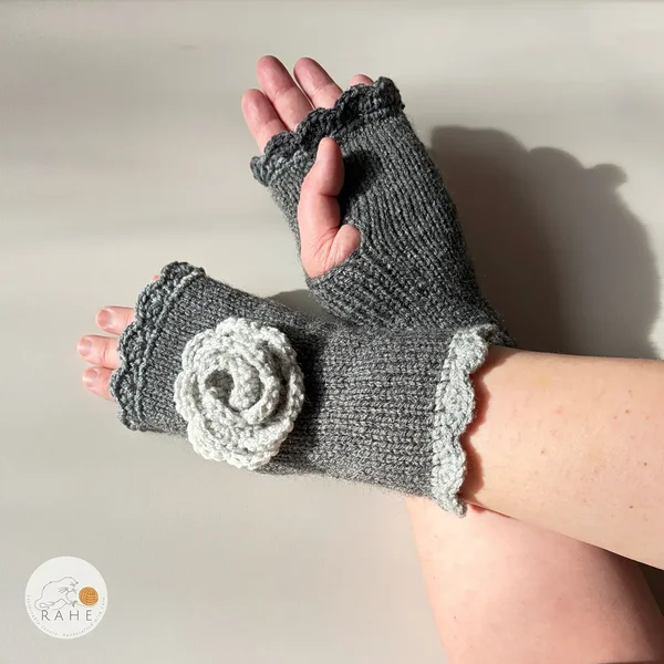 Close-up of RAHEcraft hand-knitted fingerless gloves in grey. The textured crochet flower and charcoal and light grey lace edging create a romantic and feminine look.