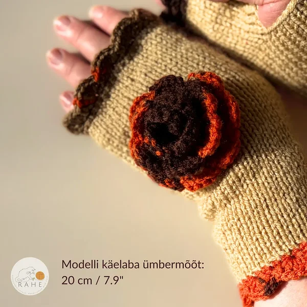 RAHEcraft hand-knitted fingerless glove inbeige with orange and brown lace edging and a crocheted flower. The image shows the fit of the glove on a model with a hand circumference of 20 cm (7.9").