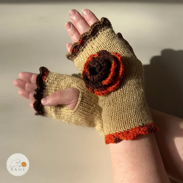 Close-up of RAHEcraft hand-knitted fingerless gloves in beige. The textured crochet flower and orange-brown lace edging create a romantic and feminine look.