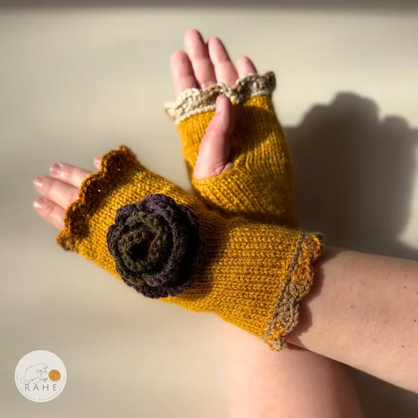Hand-knitted mustard yellow fingerless gloves with lace edging, a crocheted flower and thumb opening, worn on a model – Nordic autumn inspired handmade design.