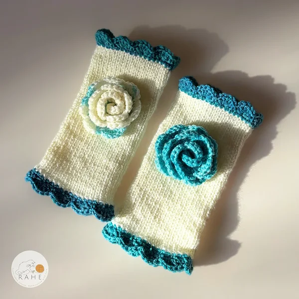 Pair of RAHEcraft hand-knitted fingerless gloves in ivory white with deep teal lace edging and a textured crocheted flower.