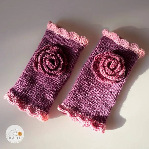 Pair of RAHEcraft hand-knitted fingerless gloves in berry pink with soft pink lace edging and a textured crocheted flower.