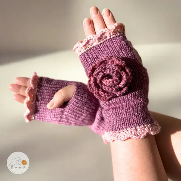 RAHEcraft hand-knitted fingerless gloves in berry pink decorated with a crocheted flower and soft pink lace edging. The smooth knit creates a romantic handmade accessory.
