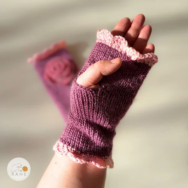 RAHEcraft hand-knitted fingerless gloves in berry pink with soft pink lace edging and a crocheted flower. The smooth knit keeps wrists warm and adds a romantic handmade touch.