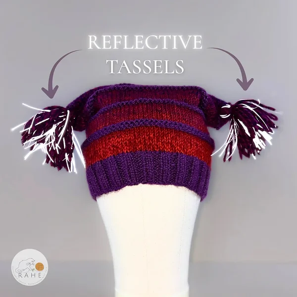 RAHEcraft hand-knitted reflective beanie with purple and red striped knit pattern, shown on a mannequin with reflective tassels for added visibility. Estonian handicraft gift.
