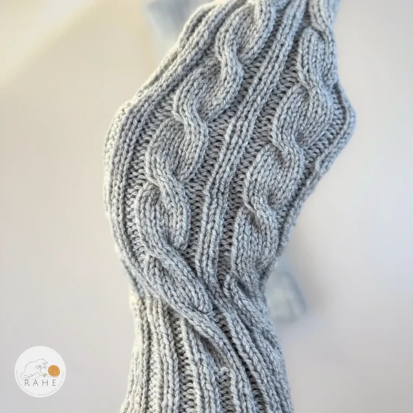 Close-up of RAHEcraft hand-knitted cable knit leg warmers in soft light grey yarn. The detailed knit texture shows the classic cable pattern. Available in three sizes: Adult, Teen and Kid.