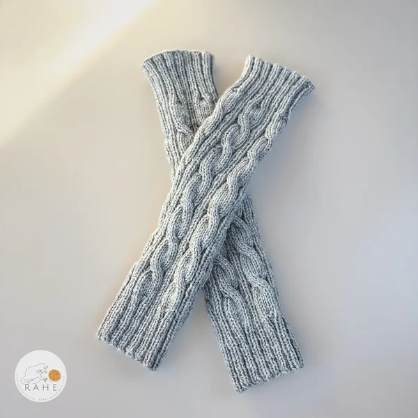 Light grey hand-knitted cable knit leg warmers by RAHEcraft laid flat to show the texture and shape. Cozy winter accessory available in Adult, Teen and Kid sizes.