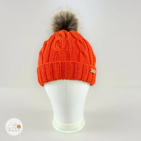 Front view of an orange hand-knitted merino wool children’s hat with faux fur pom-pom by RAHEcraft