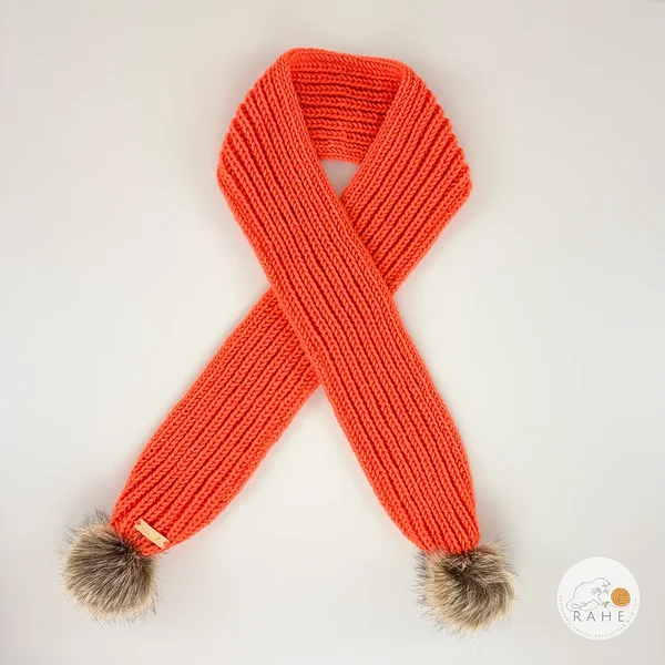 Orange hand-knitted merino wool scarf with a faux fur pom-pom, rolled view