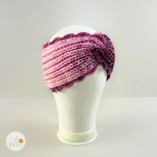 Hand-knitted wide acrylic headband in gradient white, pink, and purple, fisherman’s knit with hand-crocheted scalloped edge, side view on mannequin, RAHEcraft