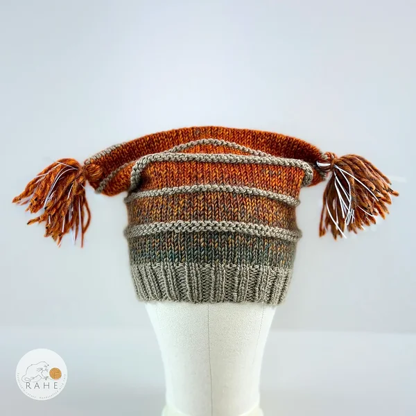 Side view of a hand-knitted reflective tassel hat in warm orange and beige tones