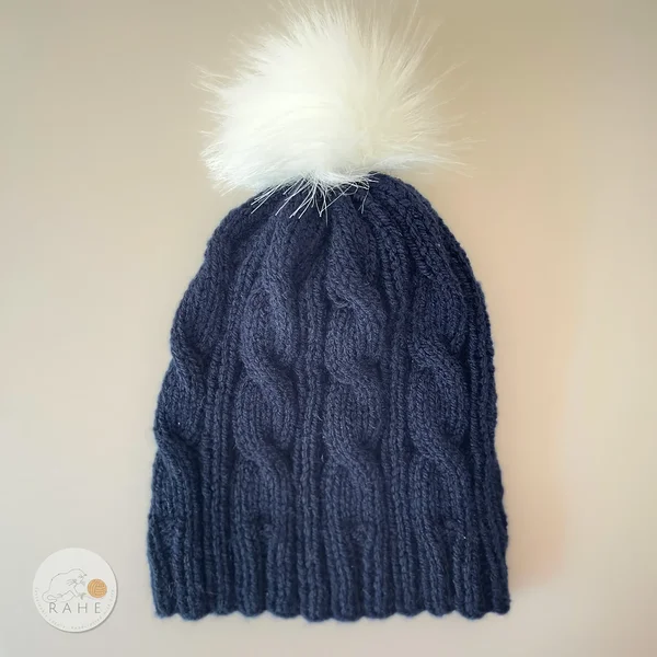 Blue handknit beanie, classic cable knit pattern, animal friendly white faux fur pom, made by RAHEcraft